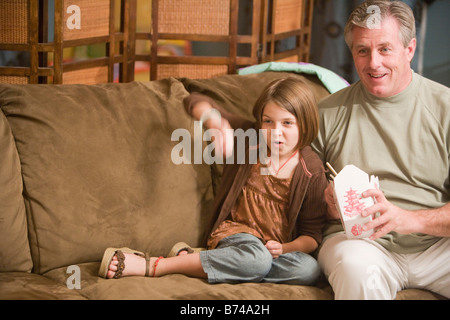 Le père et l'enfant assis sur le divan à regarder la télévision pour emporter l'alimentation Banque D'Images