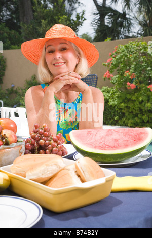 Mature Woman sitting at table avec des fruits et du pain par piscine Banque D'Images