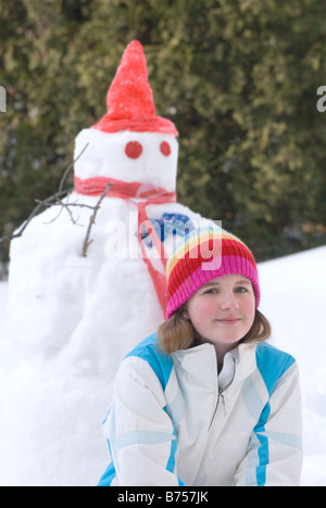 Treize ans, fille agenouillée à côté de snowman, Winnipeg, Canada Banque D'Images