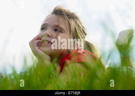 Fillette de six ans avec le menton dans les mains lying on grass, Winnipeg, Canada Banque D'Images