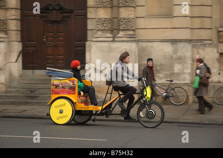 Un guide d'Oxford conduisant un taxi tricycle jaune avec de la publicité pour une production de Creation Theatre Company sur High Street, Oxford, Angleterre, Royaume-Uni Banque D'Images