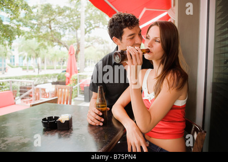 Jeune femme à boire de la bière avec un jeune homme assis à côté d'elle et souriant Banque D'Images