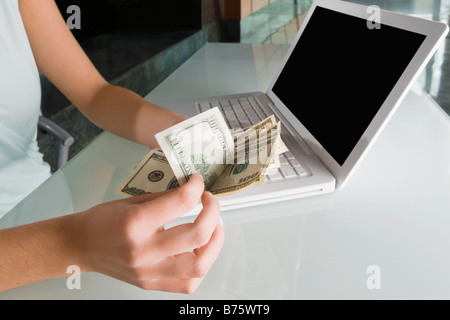 Mid section view of a businesswoman comptant du papier-monnaie en face d'un ordinateur portable Banque D'Images