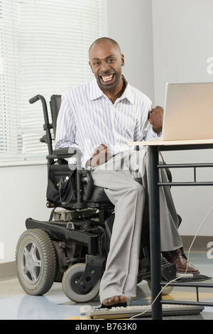 Portrait d'un homme souffrant de paralysie cérébrale dans un fauteuil roulant et travaillant sur un ordinateur avec son pied Banque D'Images