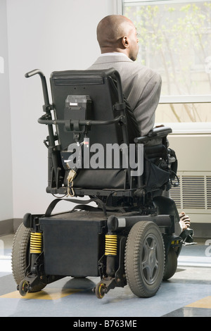 Businessman with Cerebral Palsy assis dans un fauteuil roulant et à la recherche dans le cadre d'une fenêtre Banque D'Images