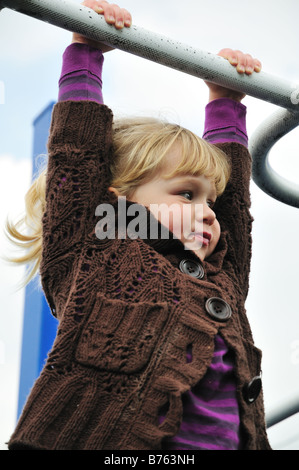 Une petite fille joyeuse pend du monkey bars à une cour d'école Banque D'Images