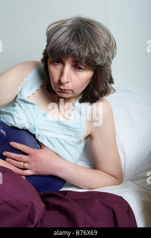 Femme d'âge moyen au lit holding bouteille d'eau chaude à l'estomac de sensation de malaise et sur le point d'être malade Banque D'Images