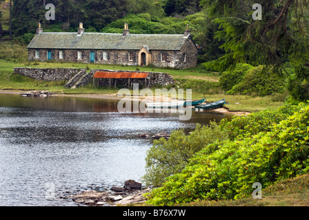 Chalets en pierre près du loch Ordie lointain près de Dunkeld, en Écosse, avec des bateaux à rames et des rhododendrons le long du rivage. Banque D'Images
