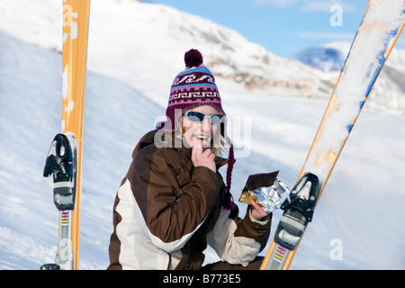 Young woman eating chocolate bar sur la neige