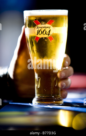 Pinte de bière Kronenbourg 1664 produit par groupe Carlsberg étant détenu par une main à un comptoir de bar. Banque D'Images