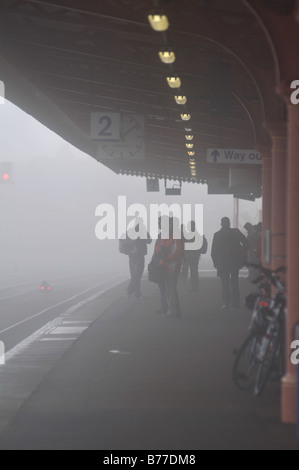 Les passagers qui attendent sur le quai de la station de chemin de fer en hiver brouillard, UK Banque D'Images