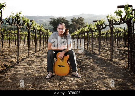 Musicien assis dans vignoble avec guitare, style de portrait. Banque D'Images