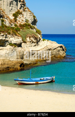Bateau de pêche sur une plage avec de l'eau bleu clair ci-dessous les falaises escarpées, Tropea, Vibo Valentia, Calabre, en mer Tyrrhénienne, au sud il Banque D'Images