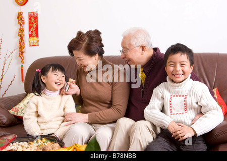 Couple avec deux enfants assis sur le canapé et souriant joyeusement Banque D'Images