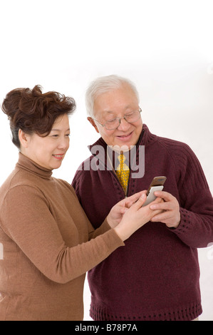 Couple de personnes âgées à la recherche et le mobile phone smiling heureusement Banque D'Images