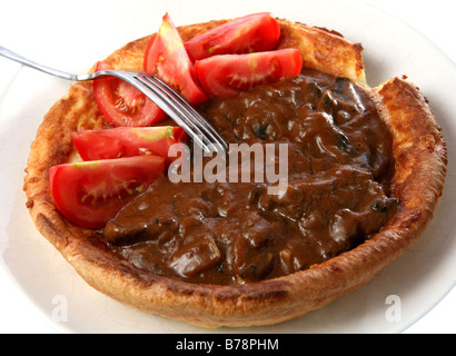 Un gros pudding Yorkshire rempli de ragoût de boeuf et champignons en sauce,complété avec des quartiers de tomate. Banque D'Images