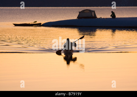 Un homme et son reflet kayak passé une femme et une tente au lever du soleil en hiver sur le lac Tahoe en Californie Banque D'Images
