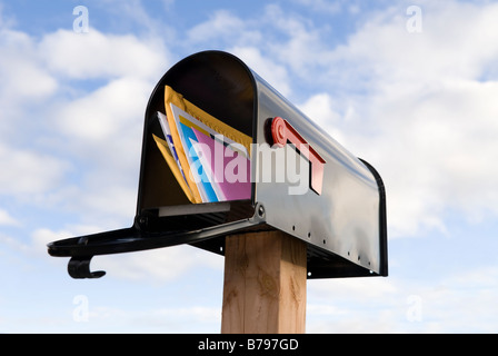 Une boîte aux lettres pleines de courrier contre un bleu et blanc ciel nuages gonflés Banque D'Images