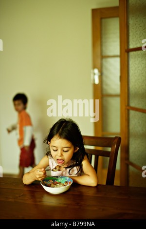 Petite fille de cinq ans est assis à une table en bois et mange un bol de céréales Banque D'Images