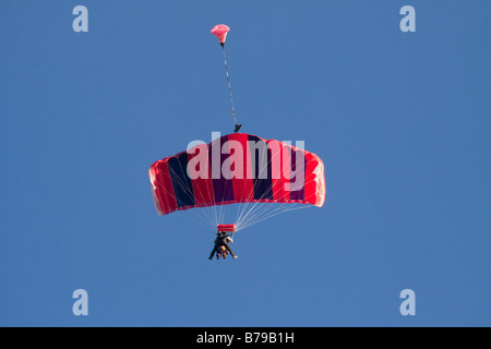 Parachutisme EN TANDEM EN ANGLETERRE Un parachute à rayures rouge transportant deux personnes GLISSE SUR LE CIEL BLEU Banque D'Images