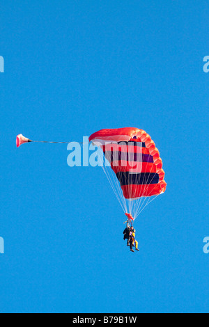 Parachutisme EN TANDEM EN ANGLETERRE Un parachute à rayures rouge transportant deux personnes GLISSE SUR LE CIEL BLEU Banque D'Images