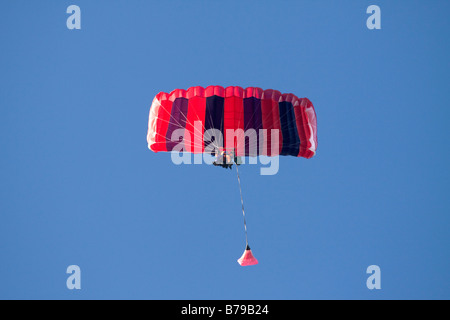 Saut en Tandem. Parachutisme EN TANDEM EN ANGLETERRE, un parachute à rayures rouge et bleu transportant deux personnes GLISSE SUR LE CIEL BLEU Banque D'Images