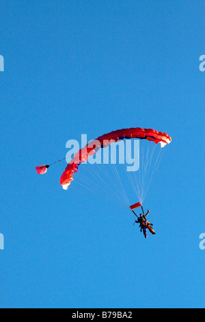 Parachutisme EN TANDEM EN ANGLETERRE Un parachute à rayures rouge transportant deux personnes GLISSE SUR LE CIEL BLEU Banque D'Images