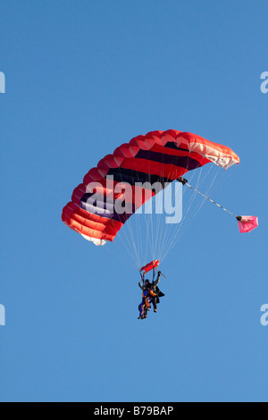 Parachutisme EN TANDEM EN ANGLETERRE Un parachute à rayures rouge transportant deux personnes GLISSE SUR LE CIEL BLEU Banque D'Images