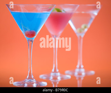 Couleur dans un verre à martini. Betty Blue, cosmopolite et Dry Martini cocktails colorés sur fond orange. Banque D'Images