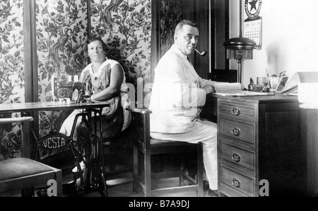 Photo historique, Couple at home, l'homme à la réception, la femme à la machine à coudre, ca. 1920 Banque D'Images