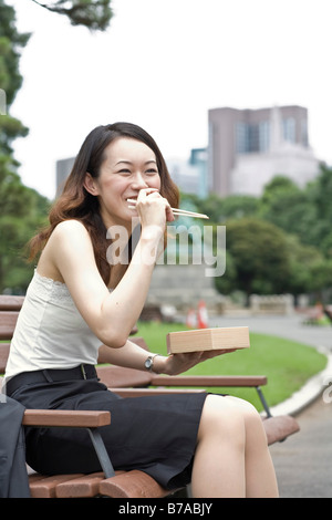 Jeune femme en riant tout en mangeant le déjeuner dans un parc de Tokyo, Japon, Asie Banque D'Images