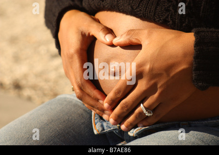 Dame enceinte dans chandail noir coeur avec les mains du ventre de formes Banque D'Images