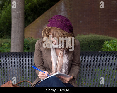 Fille sur le banc de parc écrit dans l'ordinateur portable Banque D'Images