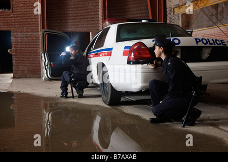 Les agents de police accroupi derrière une voiture de police avec l'arme au poing Banque D'Images