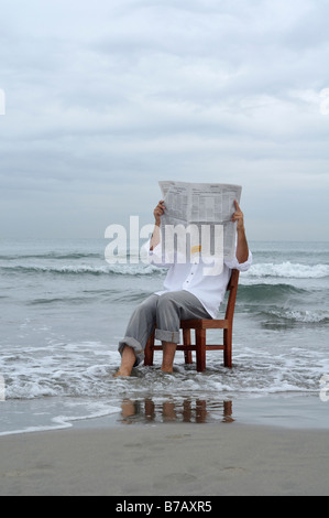 L'homme assis sur une chaise dans l'océan lire un journal Banque D'Images