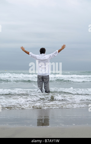 Homme debout dans les vagues sur la plage Banque D'Images