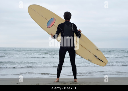 Man Holding Surfboard on Beach Banque D'Images