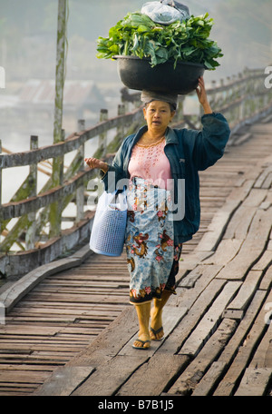 Mon femme transportant des légumes sur sa tête en bois traversant le pont en teck à Sangklaburi en Thaïlande Banque D'Images