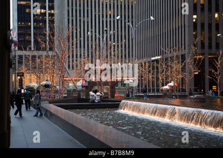 Fontaine au milieu de la rue à Manhattan avec des arbres décorés de lumières orange annonce de grands bâtiments autour de Banque D'Images