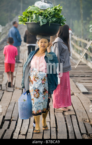 Mon femme transportant des légumes sur sa tête en bois traversant le pont en teck à Sangklaburi en Thaïlande Banque D'Images