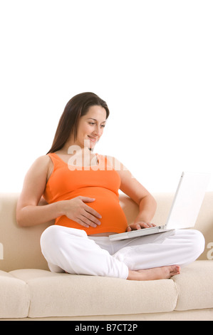 Pregnant woman sitting on sofa smiling Banque D'Images