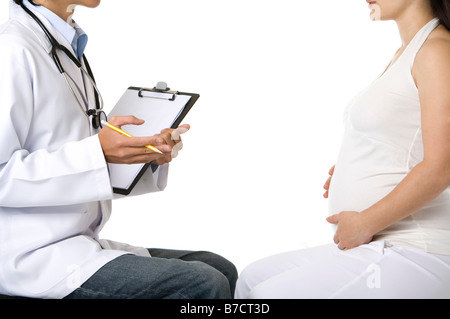 Jeune femme enceinte de toucher l'abdomen face à un médecin tenant un crayon et presse-papiers Banque D'Images