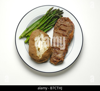 Un petit strip steak de boeuf avec asperges et une pomme de terre cuite au four avec du beurre sur une assiette blanche ronde Banque D'Images
