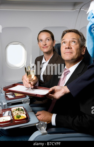 Les gens d'affaires dans un avion d'être servi des repas et champagne Banque D'Images