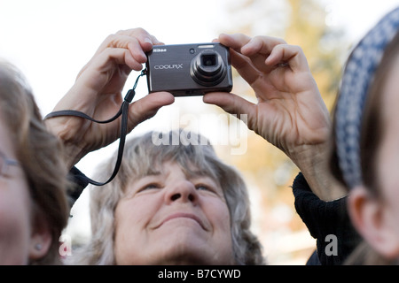 Une femme plus âgée prend une photo avec un appareil photo compact à l'événement d'inauguration à l'Université de Californie, Berkeley. Banque D'Images