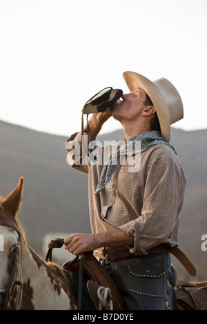 Un cowboy assis sur un cheval et boire d'une flasque Banque D'Images