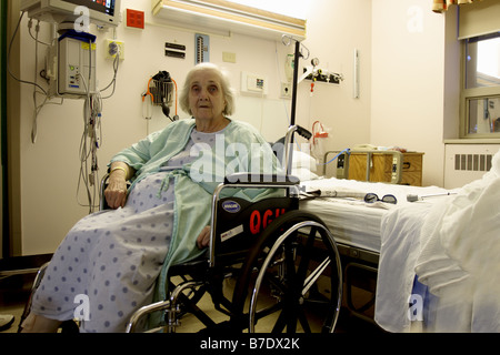 Une femme âgée dans un hôpital dans un fauteuil roulant dans sa chambre à côté de son lit Banque D'Images