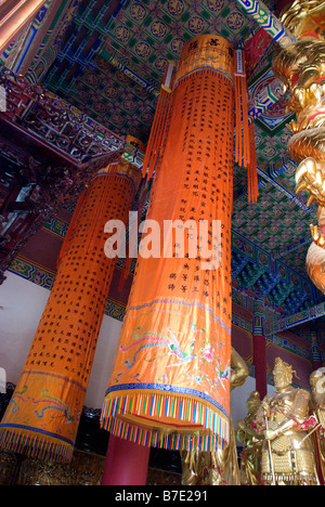 Lumineuses cylindriques-orange drapé de soie est suspendu du plafond peint bleu au milieu d'effigies d'or de dieux guerriers chinois Banque D'Images