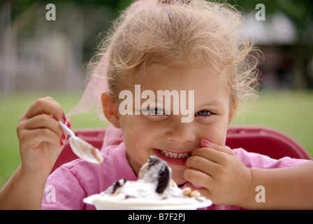 Une fillette de quatre ans biracial mange un bol de crème glacée à un pique-nique de sourire et rire. Banque D'Images