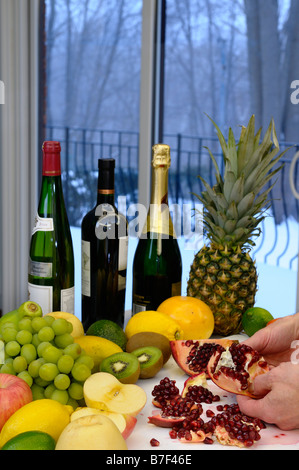 L'extraction de l'homme ouvrir une grenade entourée par des fruits et du vin dans une cuisine par une journée d'hiver Banque D'Images